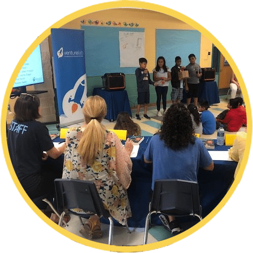 Students presenting a project in front of an audience and judges at a social entrepreneurship program event.